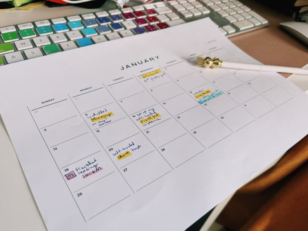 a photo showing a printout of a calendar for January 2025 with empty boxes for each day and a handful of descriptions about actions I have taken (like install Phanpy) in a color-coded way