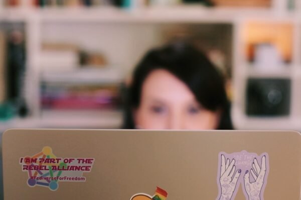 a woman with dark hair sitting behind a laptop. on the laptop lid you can see a sticker that reads "I am part of the rebel alliance"